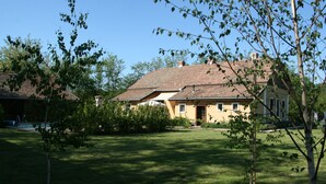 A house with a sloped roof, surrounded by a well-maintained lawn and trees. - Country house, 8 people. Private parking, swimming pool and large private garden. At Lake Tisza. (Tiszaszentimre)