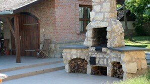 A stone-built outdoor fireplace with a firebox and steps leading up to it, set against a brick building with a wooden door and windows. - Country house, 8 people. Private parking, swimming pool and large private garden. At Lake Tisza. (Tiszaszentimre)
