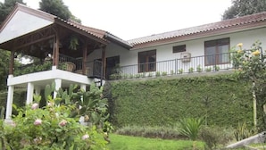 Une maison à deux étages dotée d’un porche abrité et d’un jardin où poussent diverses plantes et fleurs.
