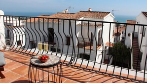 Une terrasse avec une table, deux verres de vin blanc et un saladier de fruits.