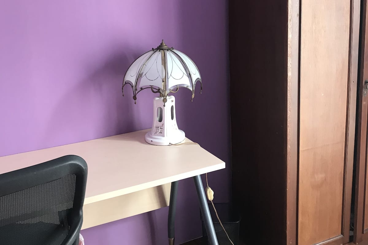 A room with a purple wall, a white desk, and a black chair.