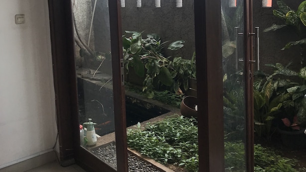 A glass door leading to a garden area with potted plants and a small water feature. - Rumah Kost (Jakarta)