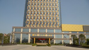 Un hotel moderno con una amplia fachada de vidrio, una entrada central con una fuente y un espacio exterior bien cuidado.