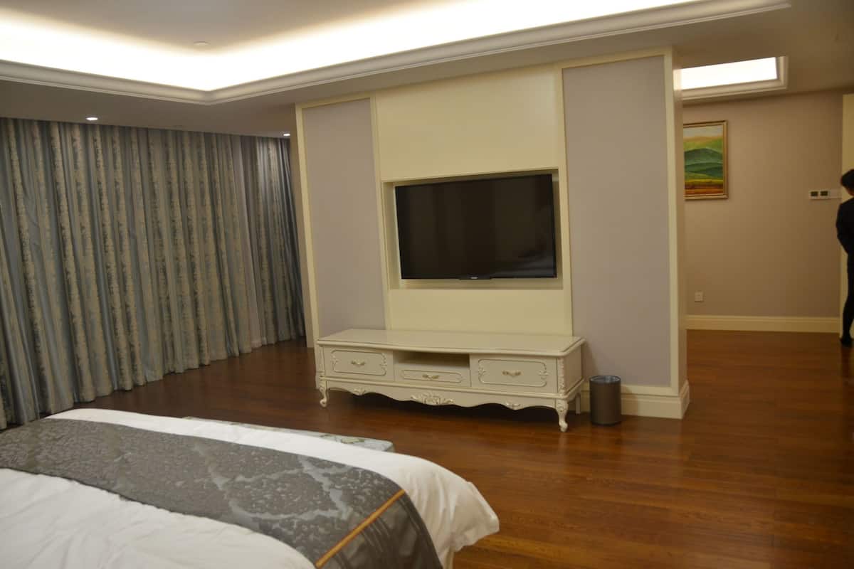 Een hotelkamer met een groot bed, een flatscreen televisie bevestigd aan een witte kast, een schilderij aan de muur en een prullenbak.