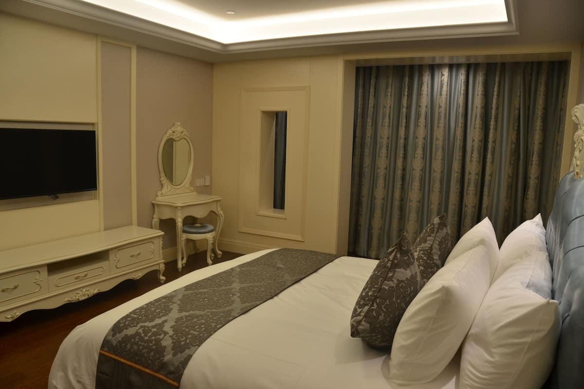 Hotelkamer met een groot bed, een televisie, een kaptafel met spiegel en een raam met gordijnen.
