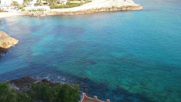 Une vue sur la côte, avec une mer bleue et limpide, un rivage rocheux et un espace piscine avec des marches descendant vers l’eau.