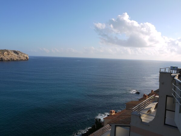 Une vue côtière avec une falaise rocheuse et un bâtiment doté d’une terrasse donnant sur la mer.