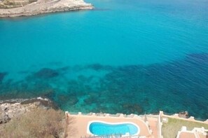 On peut clairement voir une piscine entourée d’une côte rocheuse et bordée par une mer bleue et limpide.