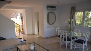Un salon moderne avec une table basse en verre, des meubles blancs et un coin repas comprenant des chaises et une table.