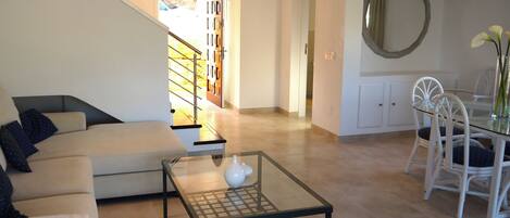 A modern living room with a sofa, a glass coffee table, and a dining area with chairs and a table.