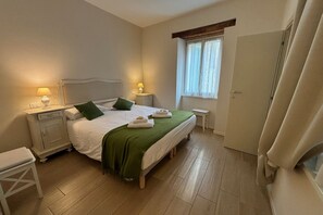 A neatly arranged bedroom with a bed, bedside tables, a nightstand, a bench, and a window with curtains.