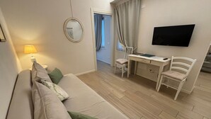 Una habitación compacta con sofá, escritorio, silla, televisor y espejo.