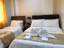 A hotel room with two beds, each with white linens and a wooden headboard. There is a nightstand with a lamp and a telephone.
