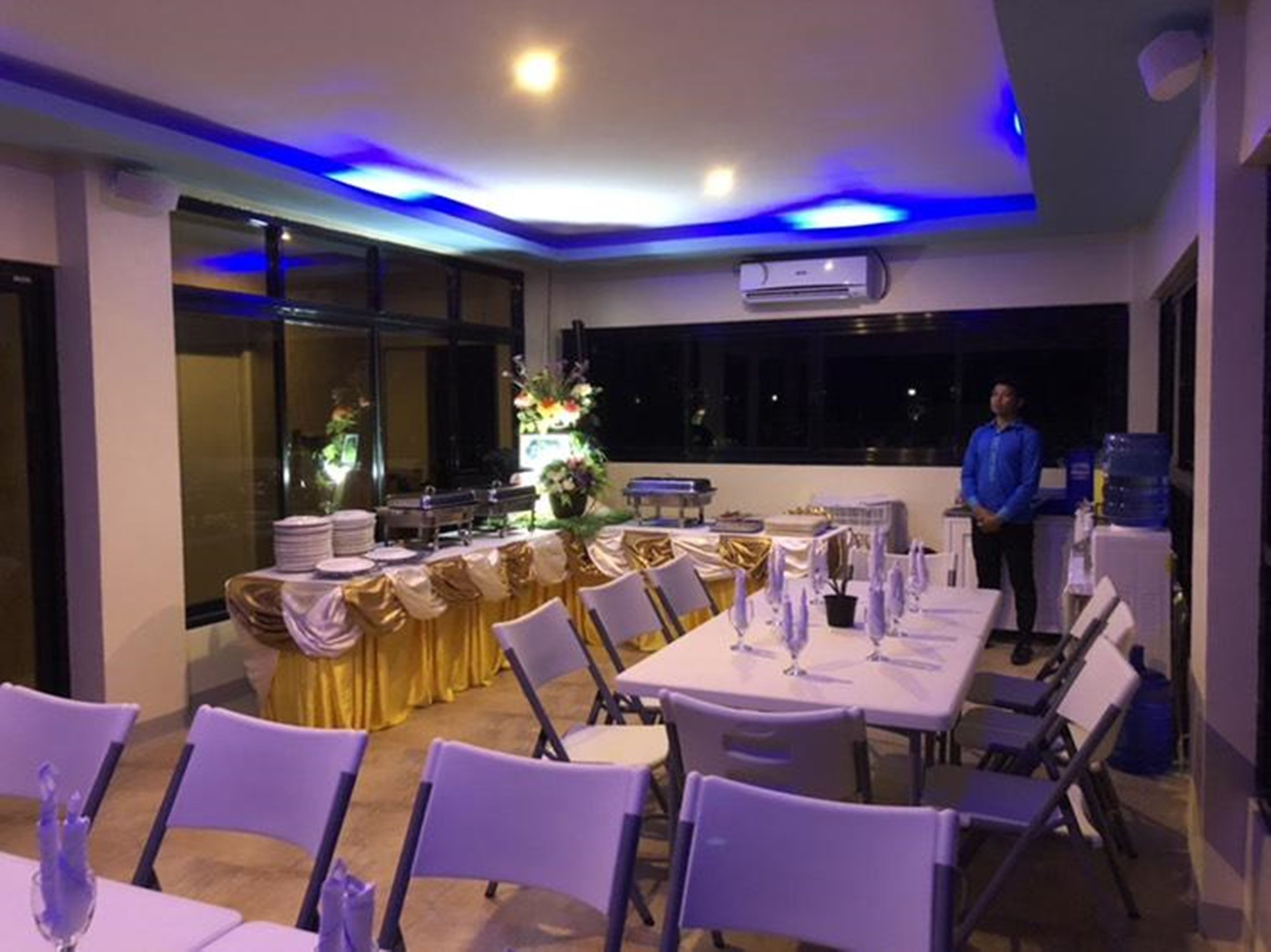A banquet hall with tables set for a formal event, featuring a ceiling with blue lighting and an air conditioning unit.