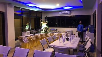 A banquet hall with tables set for a formal event, featuring a ceiling with blue lighting and an air conditioning unit.