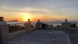 A rooftop terrace with a view of the sunset over the sea, featuring a railing and a small structure with a light. - Godo's Hotel and Restaurant (Culasi)