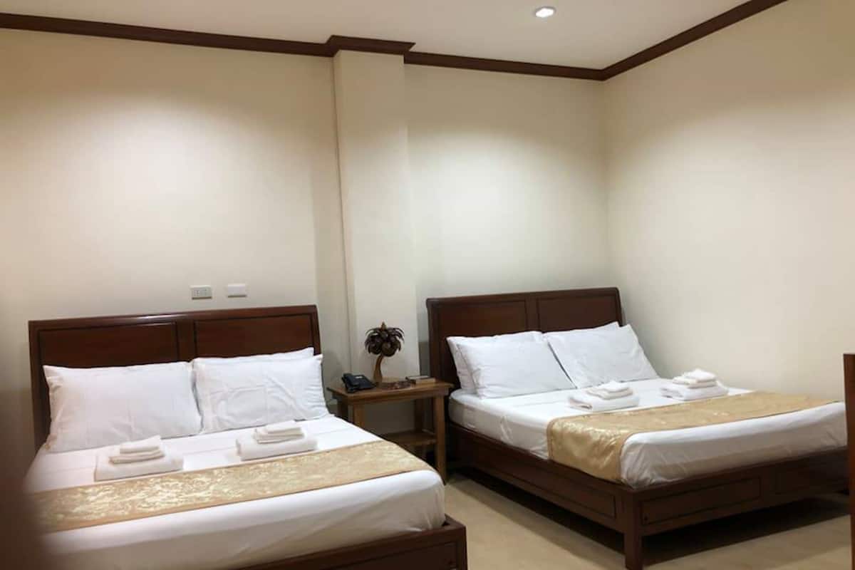 A hotel room with two single beds, each with a wooden headboard, white bedding, and a small bedside table with a lamp.