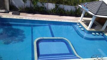 A swimming pool with a clear blue center, surrounded by a white wall and greenery.