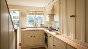 A kitchen with white cabinets, a window with a plaid blind, a stove, and a toaster. - Old Fox Cottage - sleeps 4 guests  in 2 bedrooms (Bretforton)
