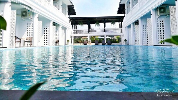 A swimming pool with a covered seating area, surrounded by white buildings with air conditioning units. - Chaanburi Boutique Resort (Chanthaburi)
