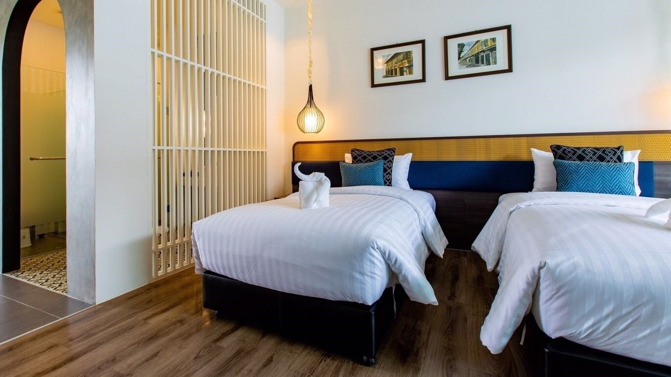 A hotel room with two beds, a wooden floor, a white partition, and a hanging light fixture.