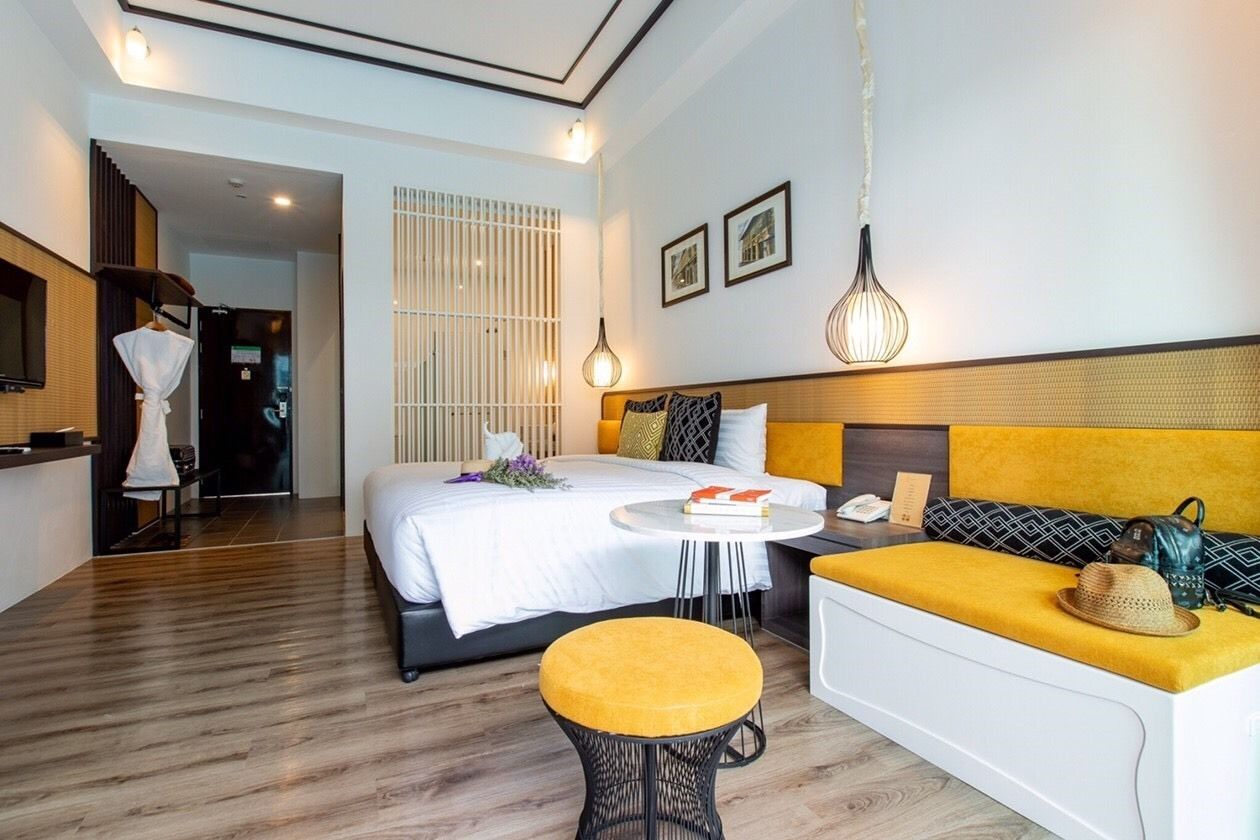 A modern hotel room with a bed, a sofa, a small table, and a hanging light fixture.