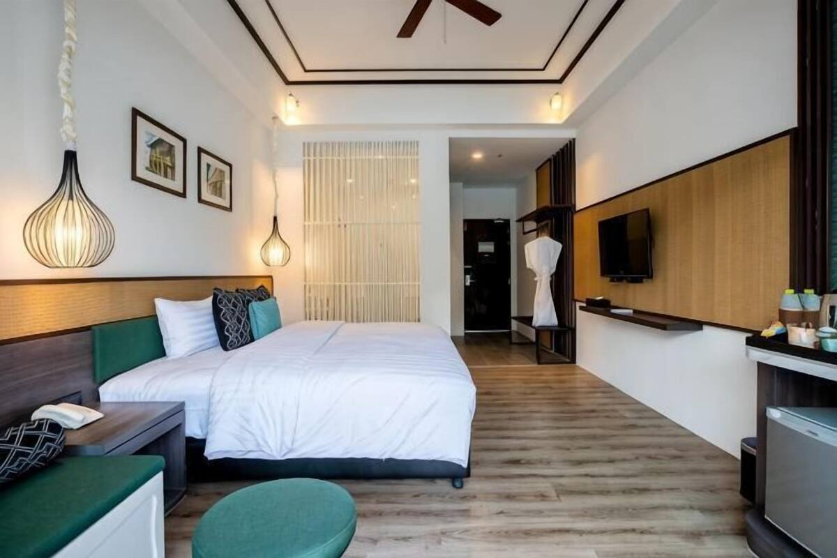 A hotel room with a bed, a desk, a TV, and a bathroom visible in the background.