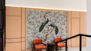 A modern interior with a staircase, two orange chairs, and a wall with a peacock design. - Aldeoz Ciater (Ciater)
