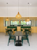 Un restaurante con una mesa central rodeada de sillas, asientos tapizados en verde y lámparas colgantes de mimbre.