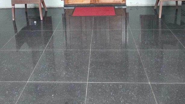 Een kamer met een grote houten deur, twee rieten stoelen en een rode mat.
