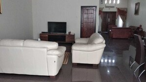 Een woonkamer met een bank, fauteuil, televisie en een houten kast.