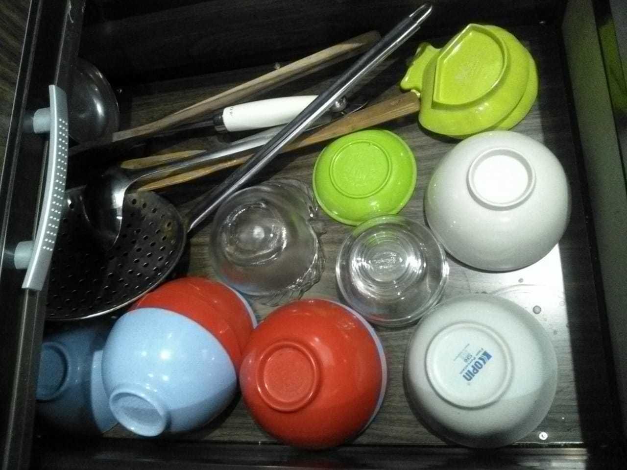 A drawer containing various kitchen utensils and containers, including a colander, spatula, and several colored lids.