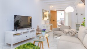 En moderne stue med et fladskærms-TV, hvide møbler, et glas sofabord og en beige sofa.
