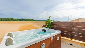Un jacuzzi con revestimiento de madera, una planta pequeña y una vista despejada del cielo y árboles distantes.