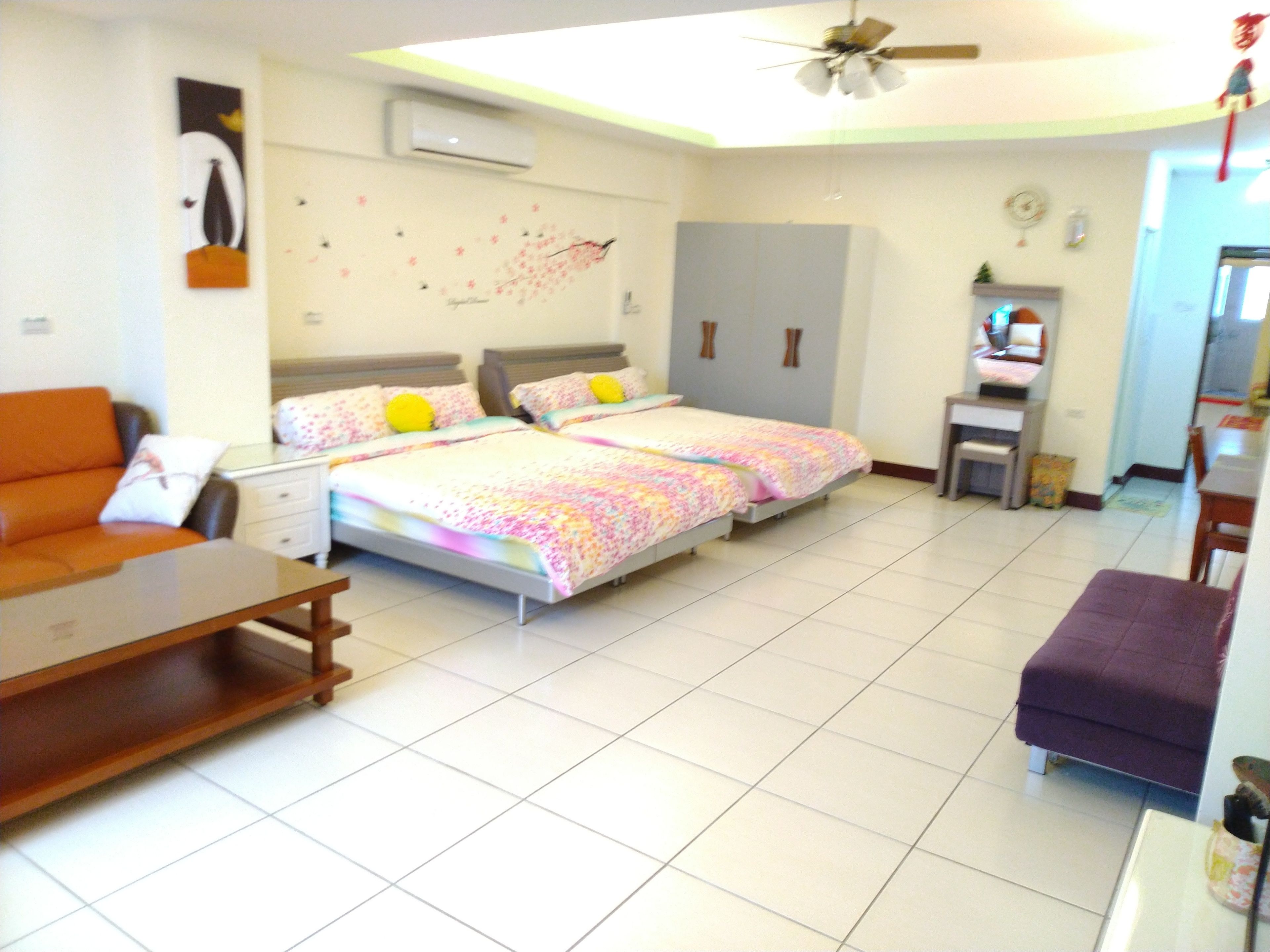 A bedroom with two beds, a sofa, a desk, and a ceiling fan.