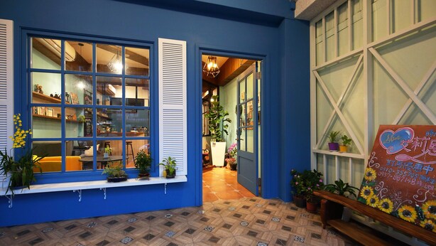 A blue exterior with large windows, a tiled floor, and a bench with potted plants.