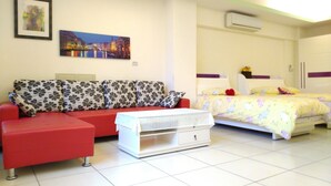 A modern bedroom with a red sofa, a white bedside table, and a double bed with floral bedding.