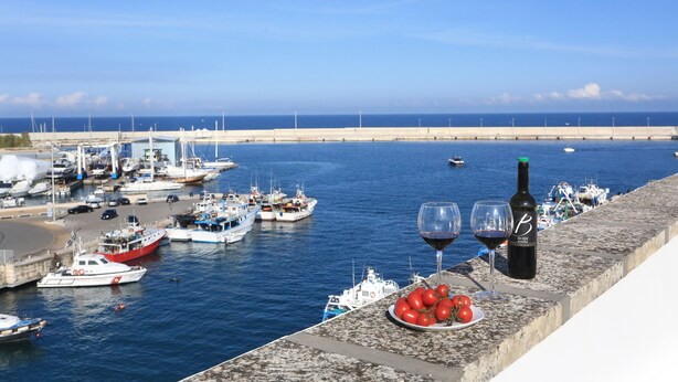 Un puerto con barcos, una botella de vino y un plato de tomates en un alféizar.