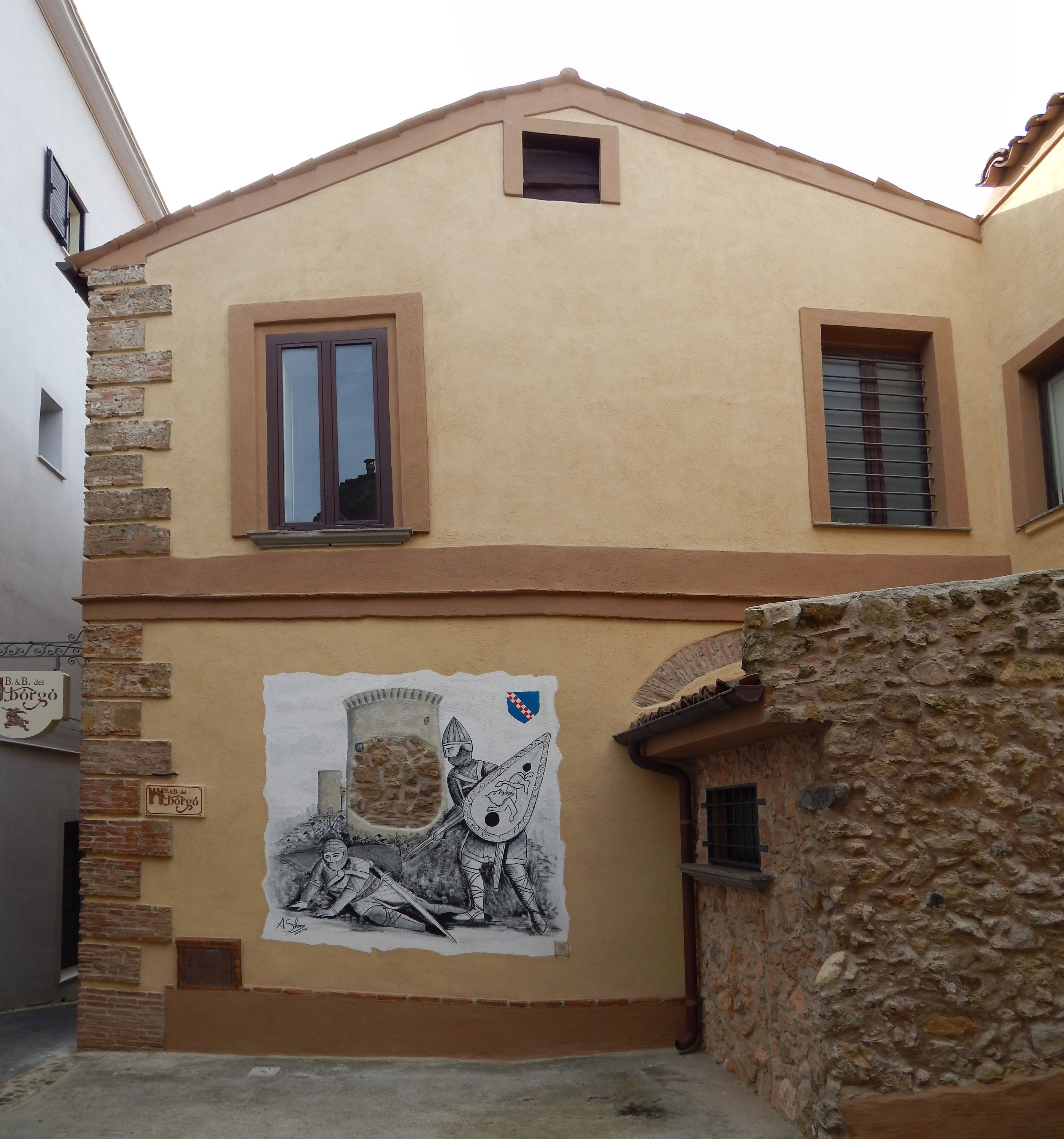 Un edificio con un mural de un caballero y un castillo, una pared de piedra y un letrero que indica B&B del borgo.