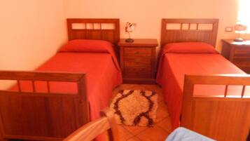 A bedroom with two single beds, wooden headboards, a small bedside table with a lamp, and a patterned rug on the floor.