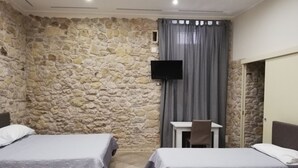 Een kamer met twee bedden, een stenen muur, een flatscreen televisie, een klein tafeltje en een deur.