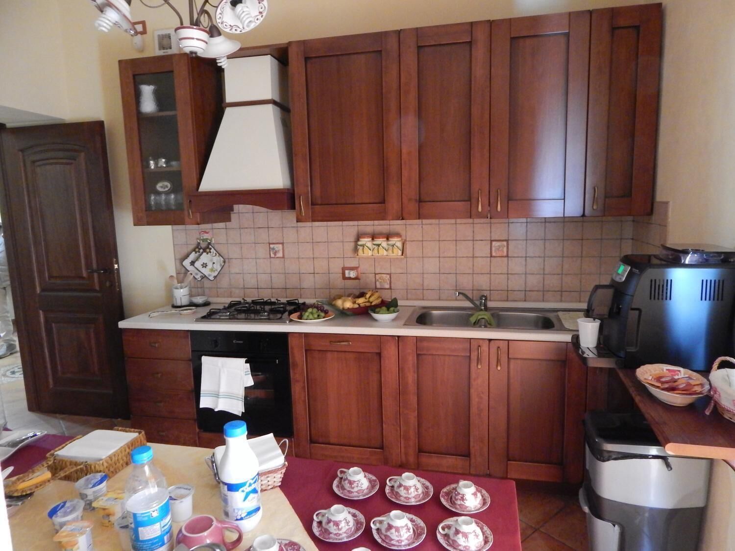 Cucina con mobili in legno, piano cottura a gas, lavello e macchina da caffè.