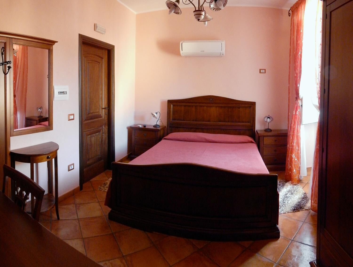 A bedroom with a wooden bed, a nightstand, a desk, a chair, a mirror, an air conditioner, and a ceiling fan.
