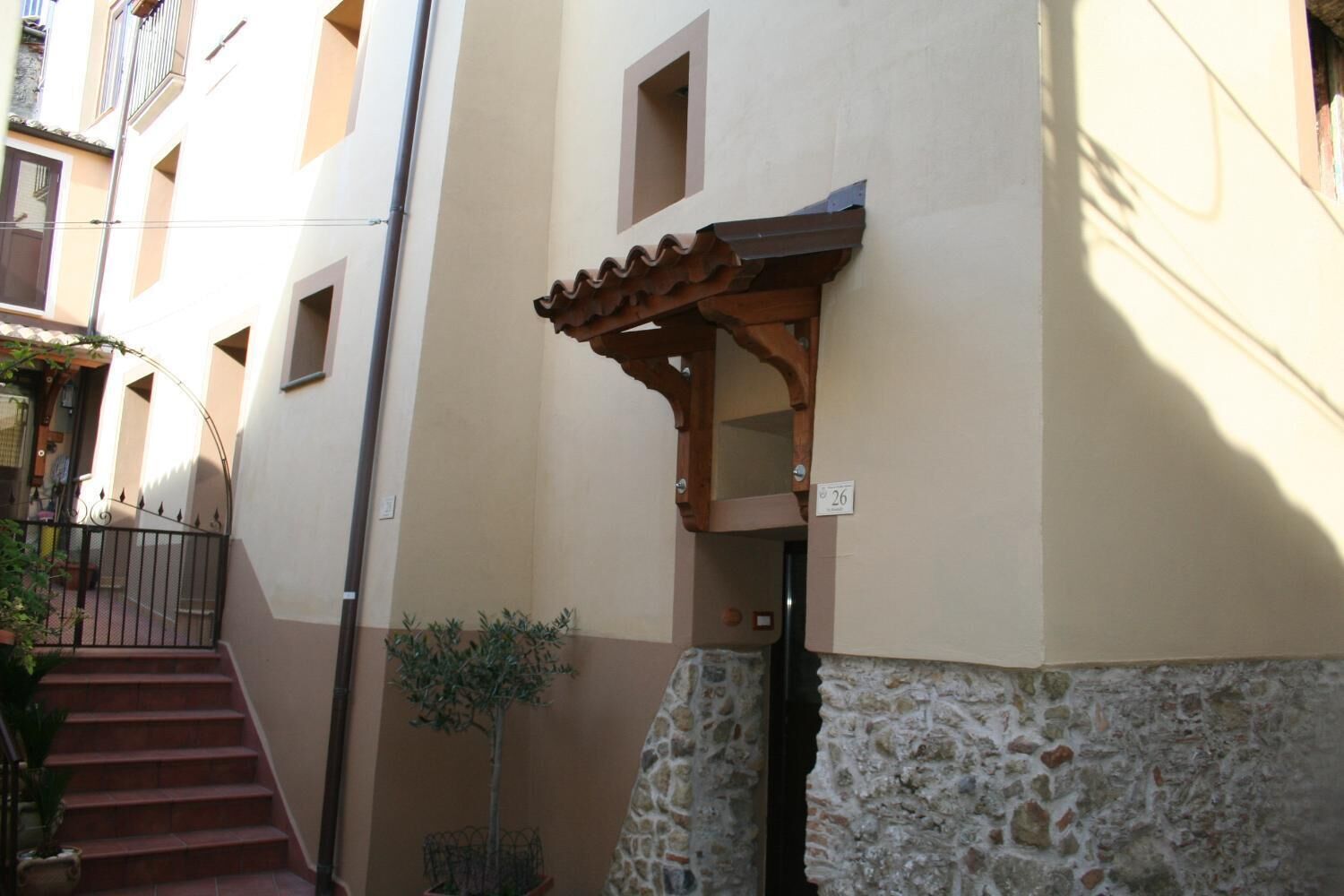 Ein schmaler Gang mit einem Pergola-Eingang, einer Steinmauer und einem Metallgitter.