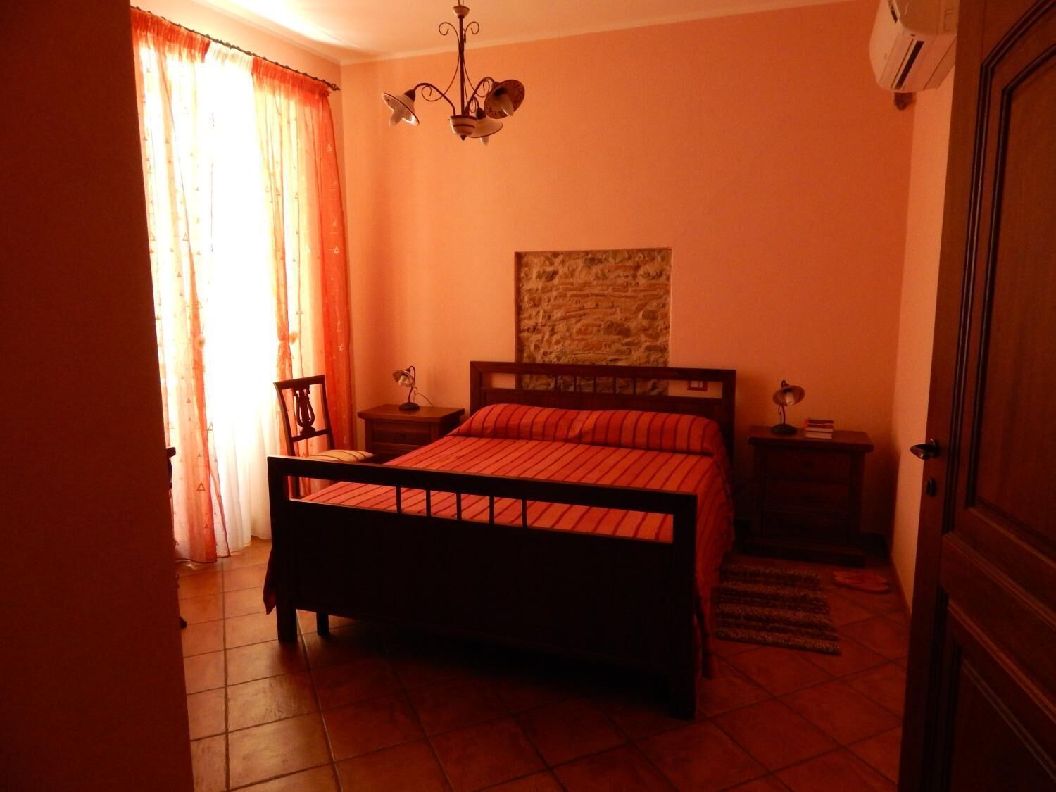 Un dormitorio con cama, mesita de noche, silla, lámpara de pared y puerta.