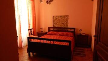 Un dormitorio con cama, mesita de noche, silla, lámpara de pared y puerta.