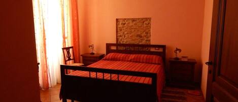 Un dormitorio con cama, mesita de noche, silla, lámpara de pared y puerta.