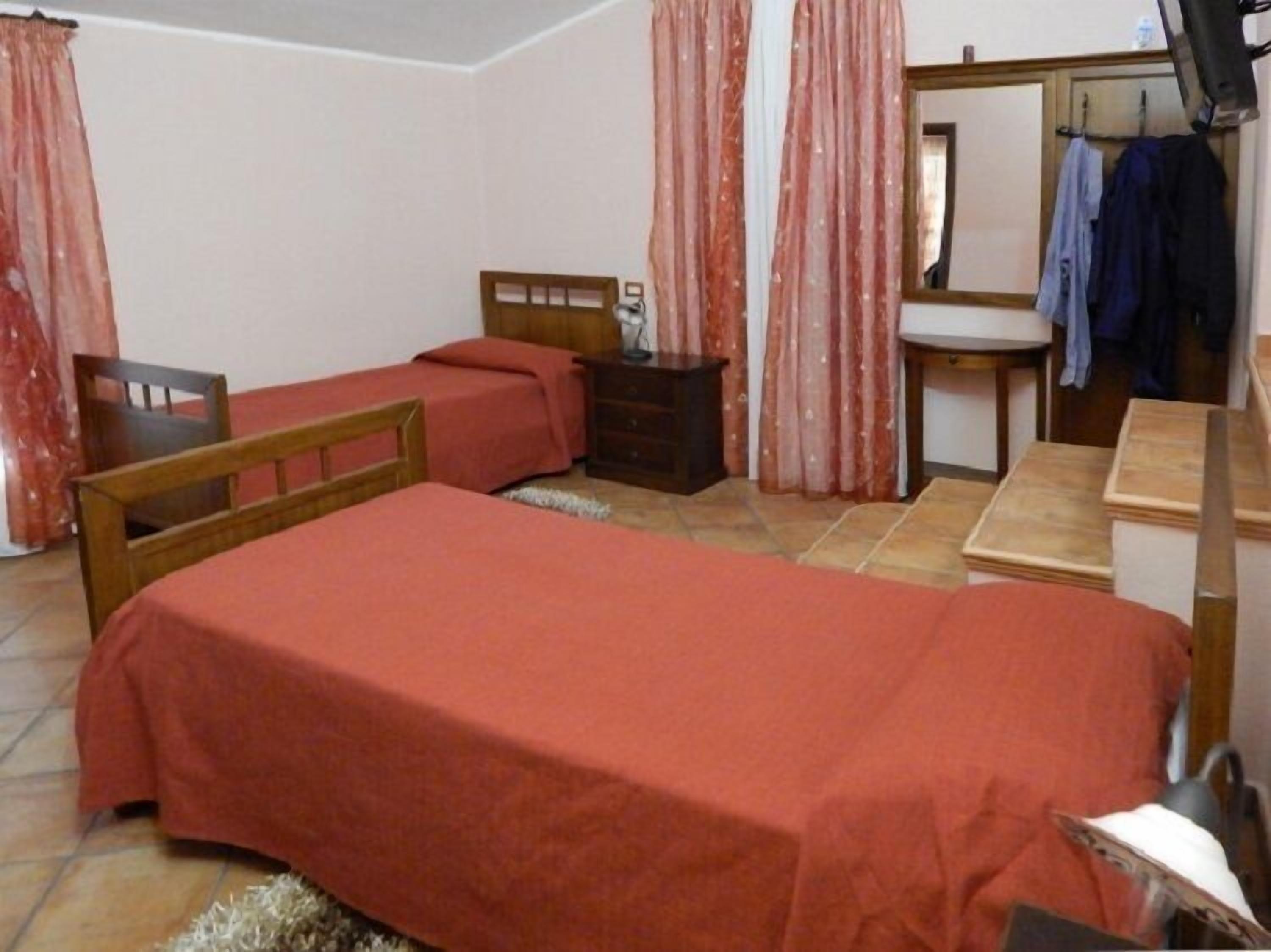 Un dormitorio con una cama individual, una silla de madera, una mesita, un espejo y un lavabo.