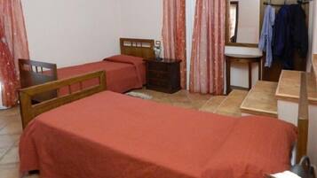 Un dormitorio con una cama individual, una silla de madera, una mesita, un espejo y un lavabo.