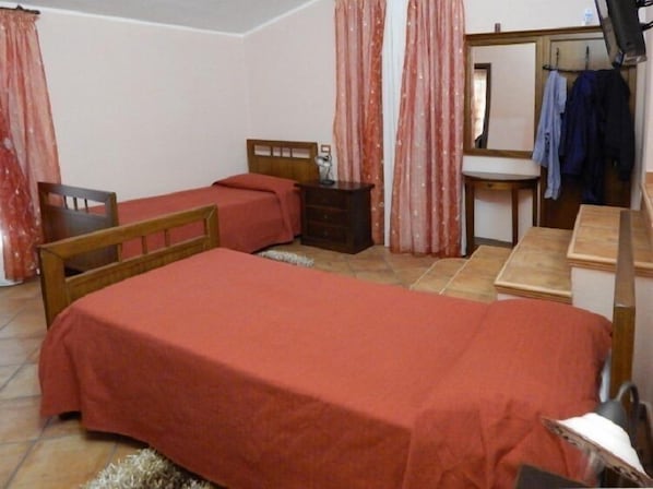 Un dormitorio con una cama individual, una silla de madera, una mesita, un espejo y un lavabo.